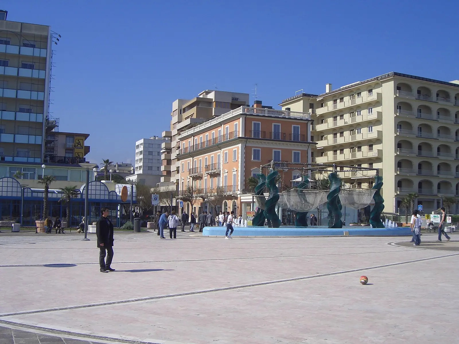 Piazzale Roma in Riccione an einem sonnigen Tag mit dem großen Skulpturenbrunnen und den umliegenden Gebäuden