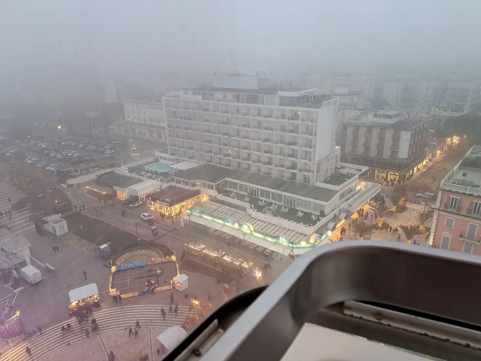 Piazzale Roma e il lungomare di Riccione visti dalla cabina della ruota panoramica nella nebbia, con le bancarelle illuminate