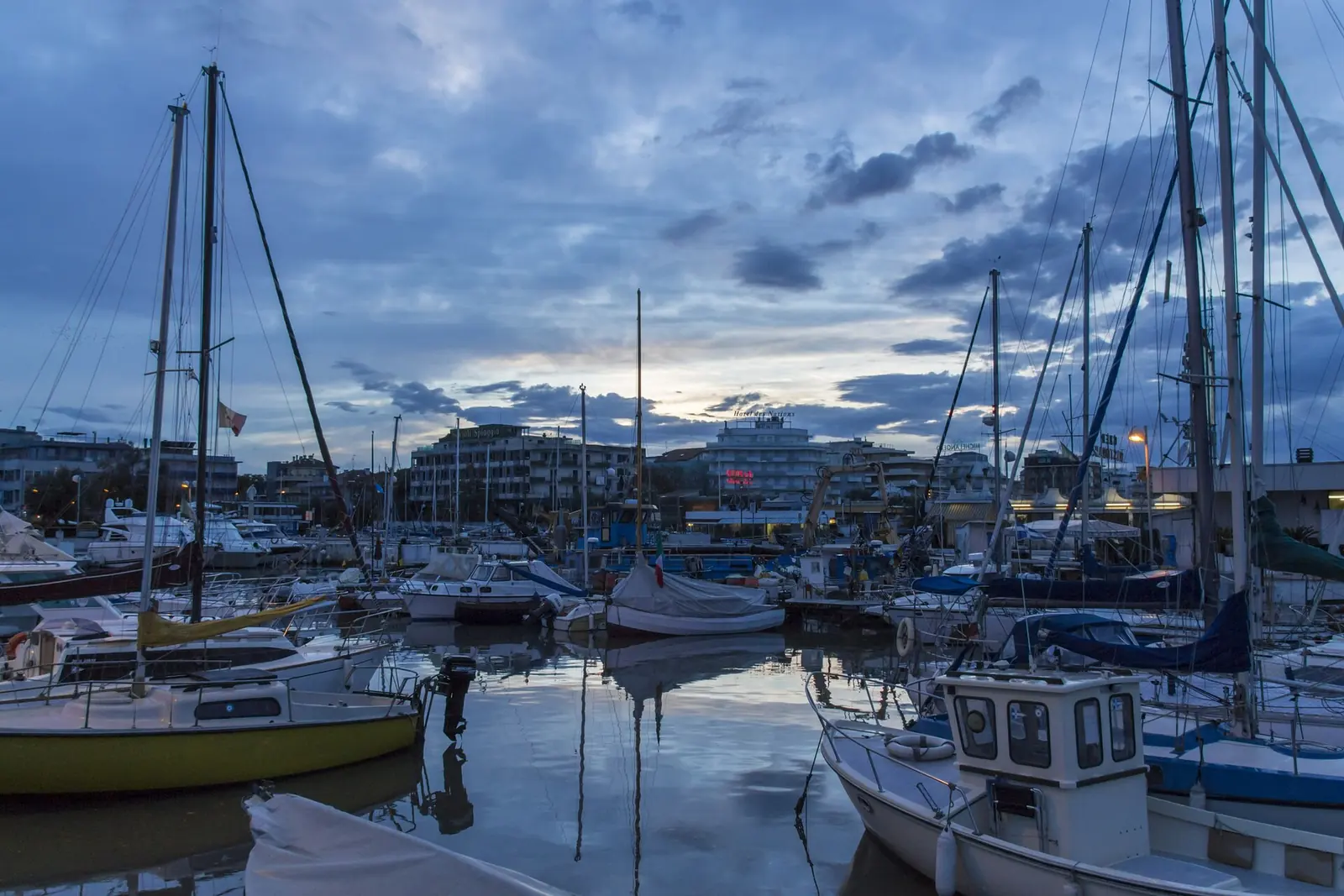 Segel- und Fischerboote im Hafen von Riccione zur blauen Stunde mit Wolkenspiegelungen im Wasser