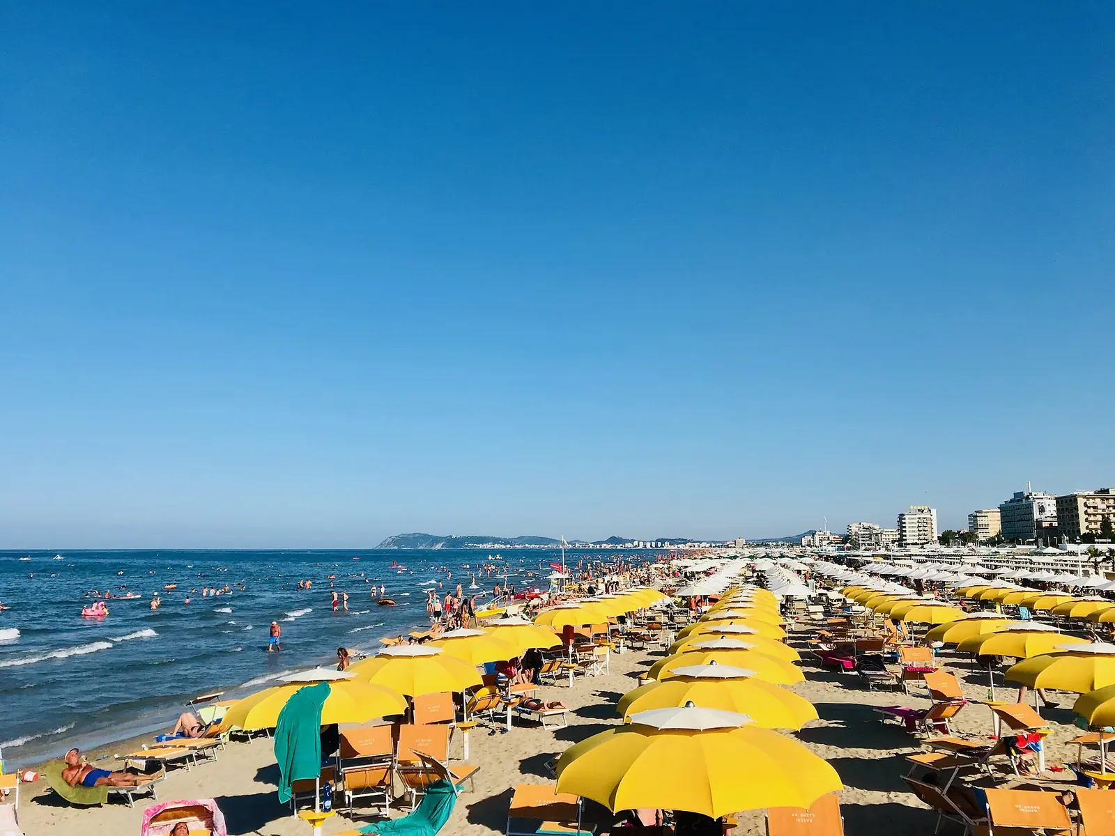 Ombrelloni gialli e sdraio sull'arenile di Riccione, con il mare mosso e il promontorio del Monte San Bartolo sullo sfondo