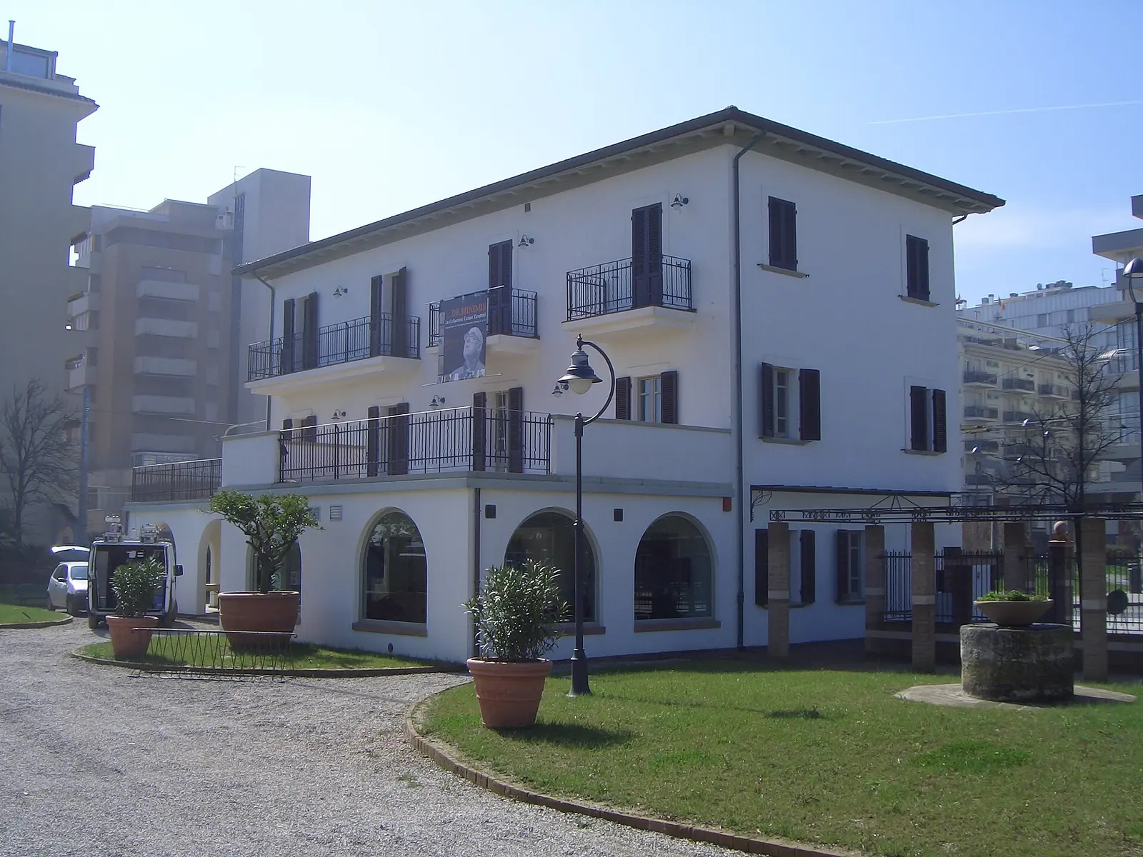 Villa Mussolini a Riccione, edificio bianco a due piani con balconi, portico ad archi e prato con vasi di piante