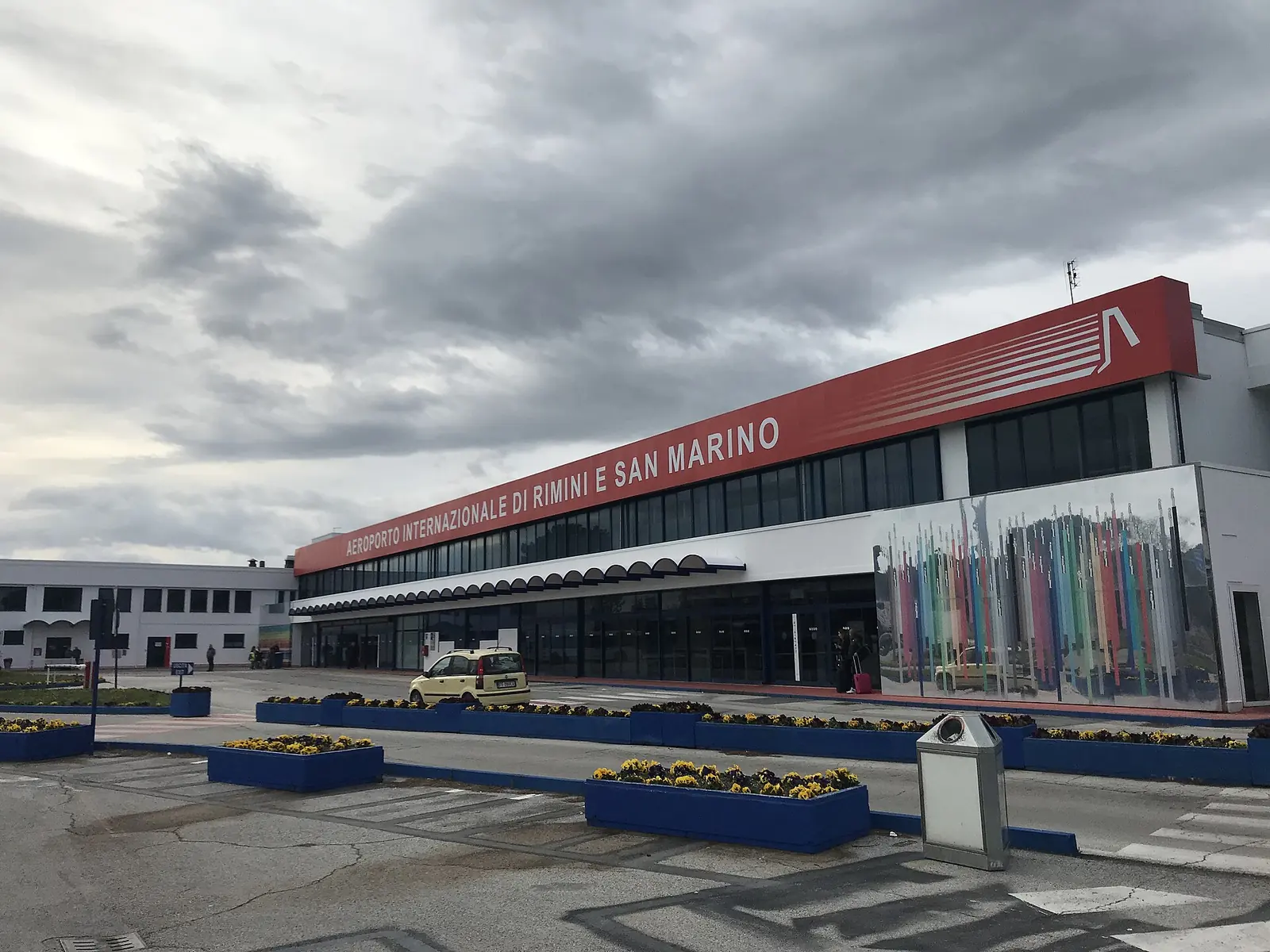 Das Gebäude des Flughafens von Rimini und San Marino mit rotem Streifen am Dach und blauen Pflanzkübeln davor