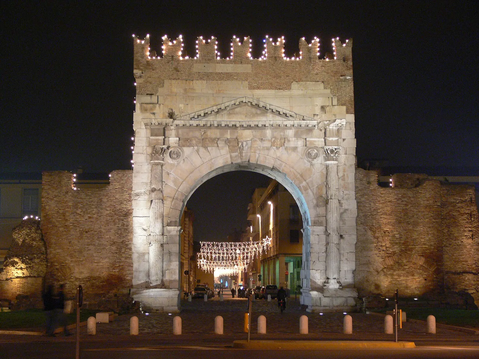 L'Arco di Augusto di Rimini di notte, con le luminarie natalizie sui merli e sulla strada che si apre oltre l'arco