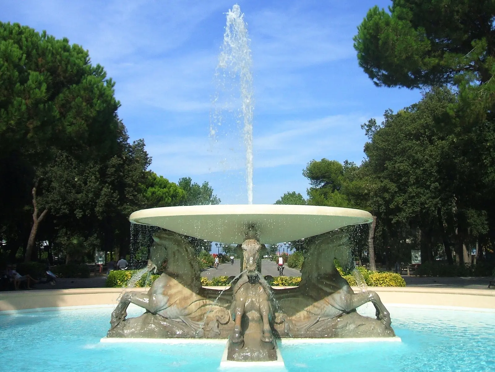 La Fontana dei Quattro Cavalli a Rimini, con il getto d'acqua al centro e i pini del parco sullo sfondo