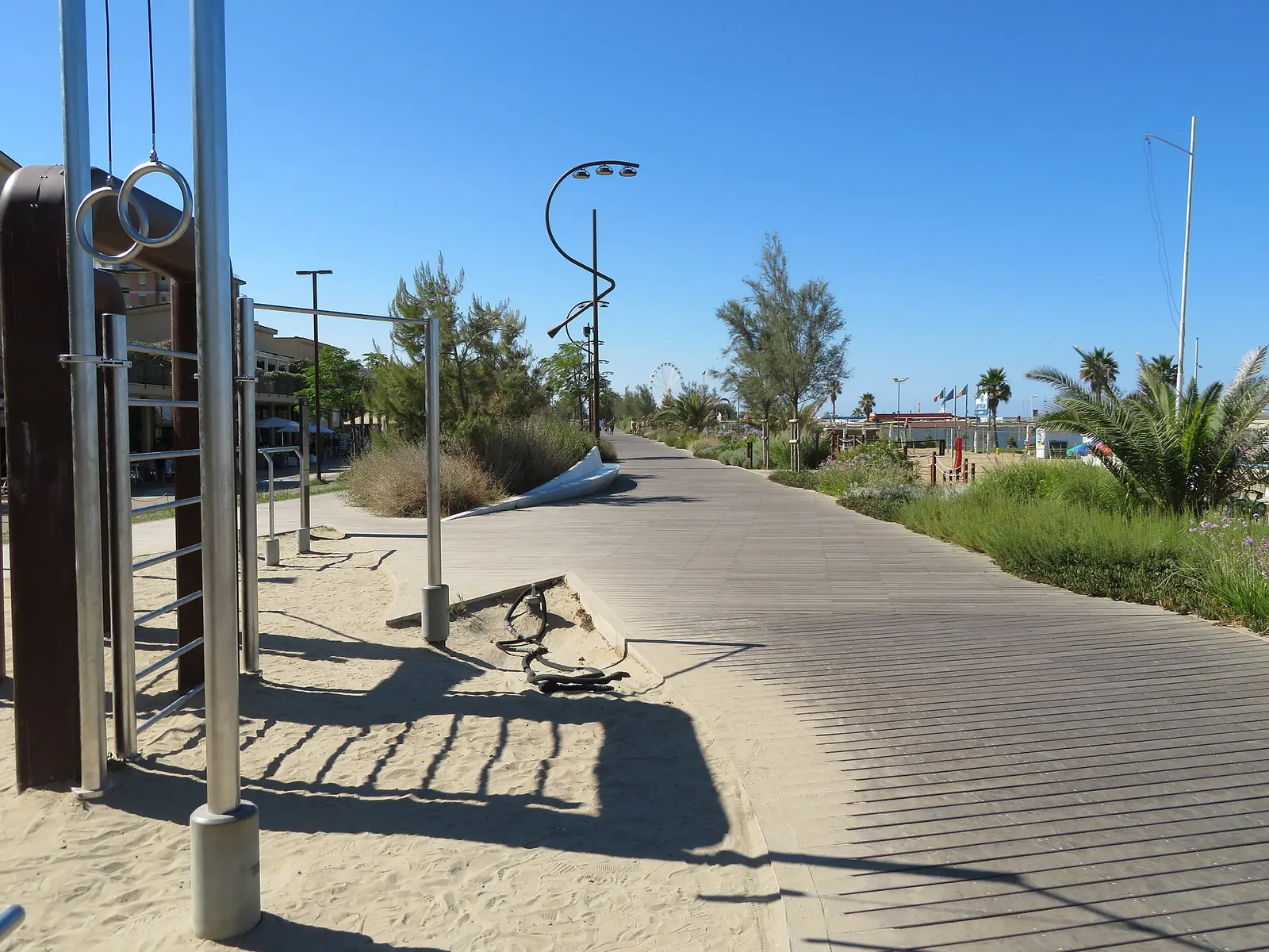 The Rimini seafront with a wooden walkway, rings and bars of an outdoor gym, and the wheel in the distance