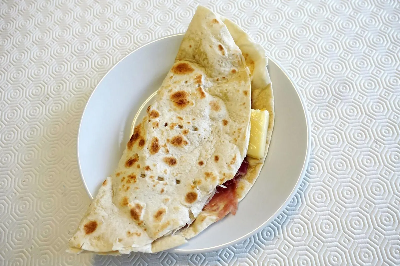 Una piadina ripiegata su un piatto bianco, con prosciutto crudo e formaggio