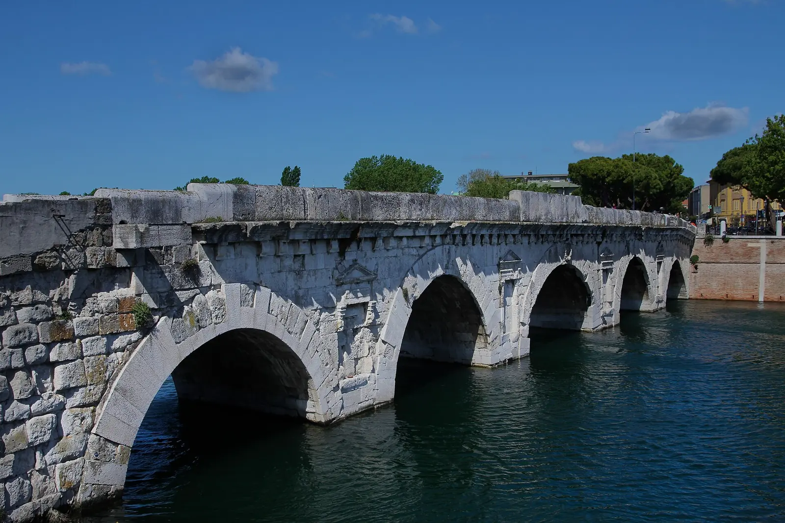 Le Ponte di Tiberio à Rimini avec ses arches en pierre blanche au-dessus de l'eau, sous un ciel bleu