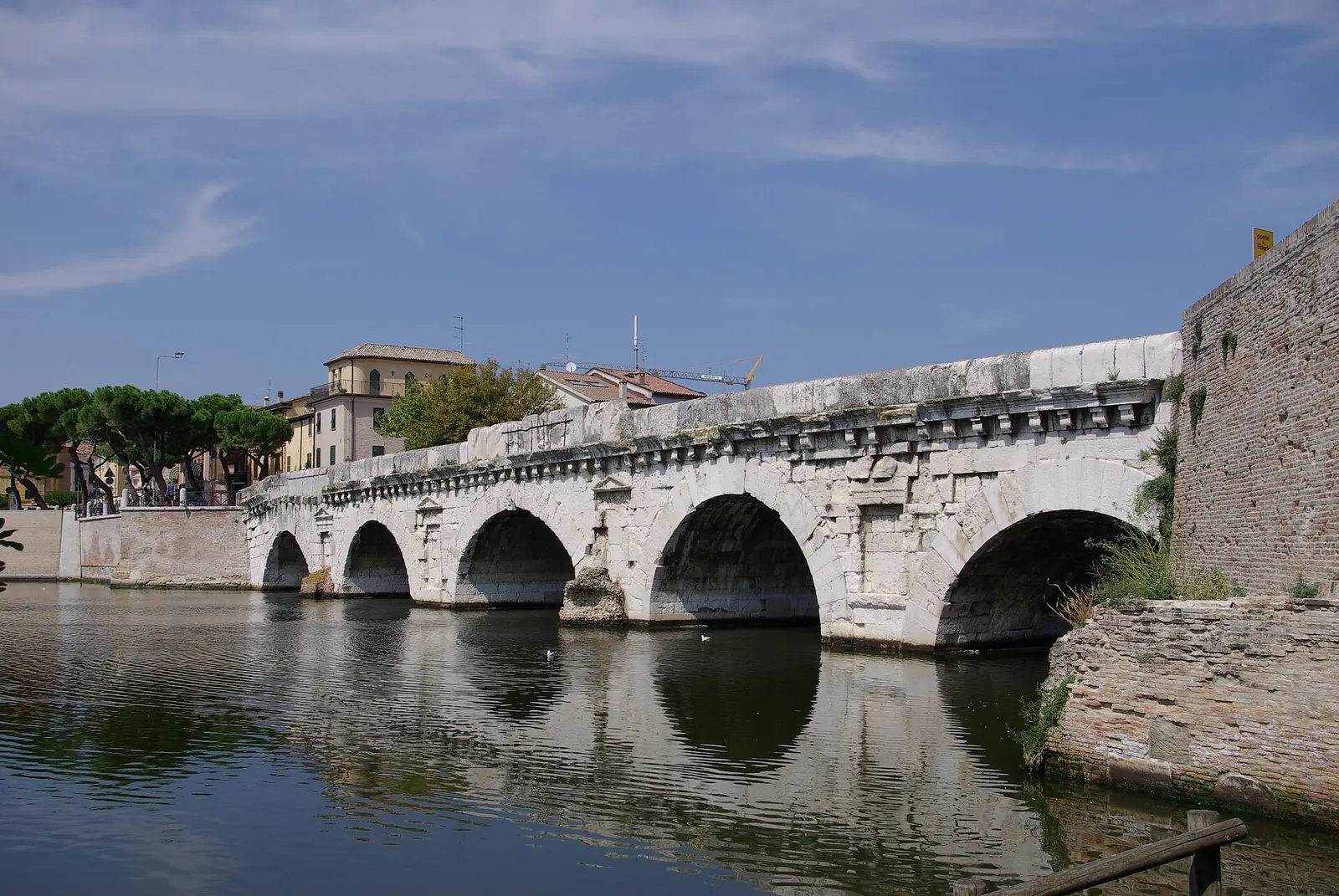 Le arcate in pietra bianca del Ponte di Tiberio a Rimini, viste dalla riva, con le case della sponda opposta