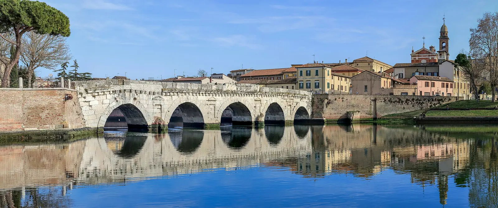 Il Ponte di Tiberio di Rimini con le arcate riflesse nell'acqua e le case colorate del Borgo San Giuliano sullo sfondo
