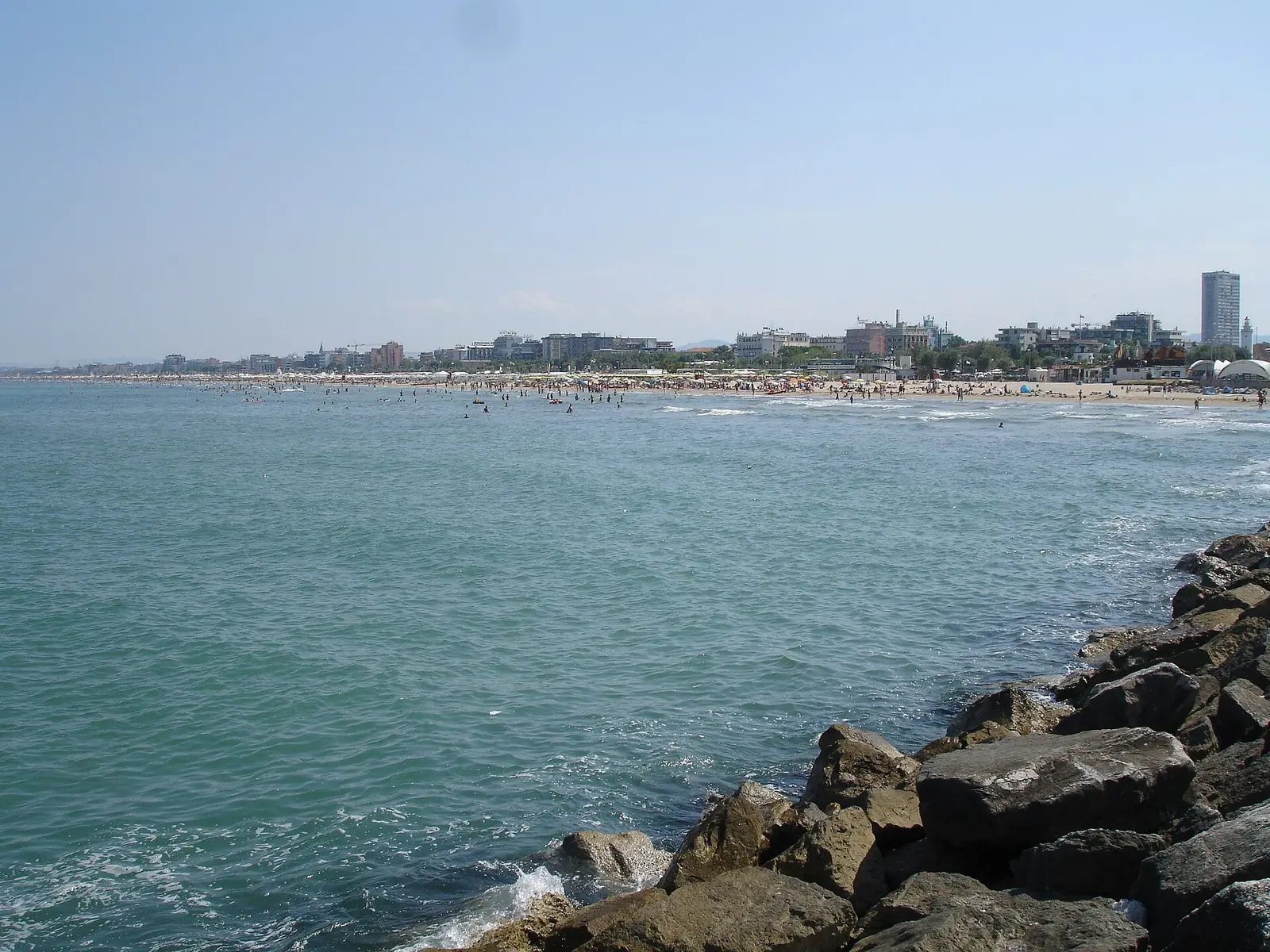 A breakwater in the foreground and, across the sea, Rimini beach with seafront buildings