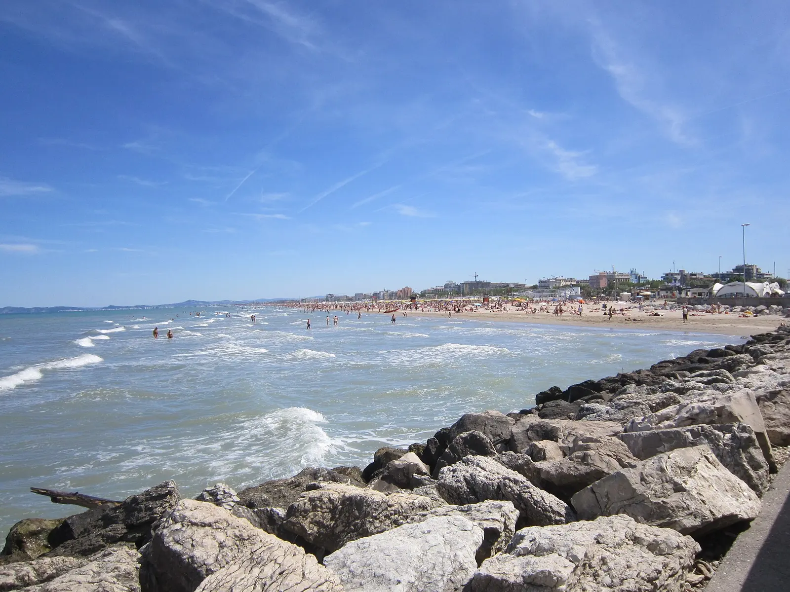 La lunga spiaggia di Rimini vista dagli scogli del molo, con i bagnanti in lontananza e la città sullo sfondo