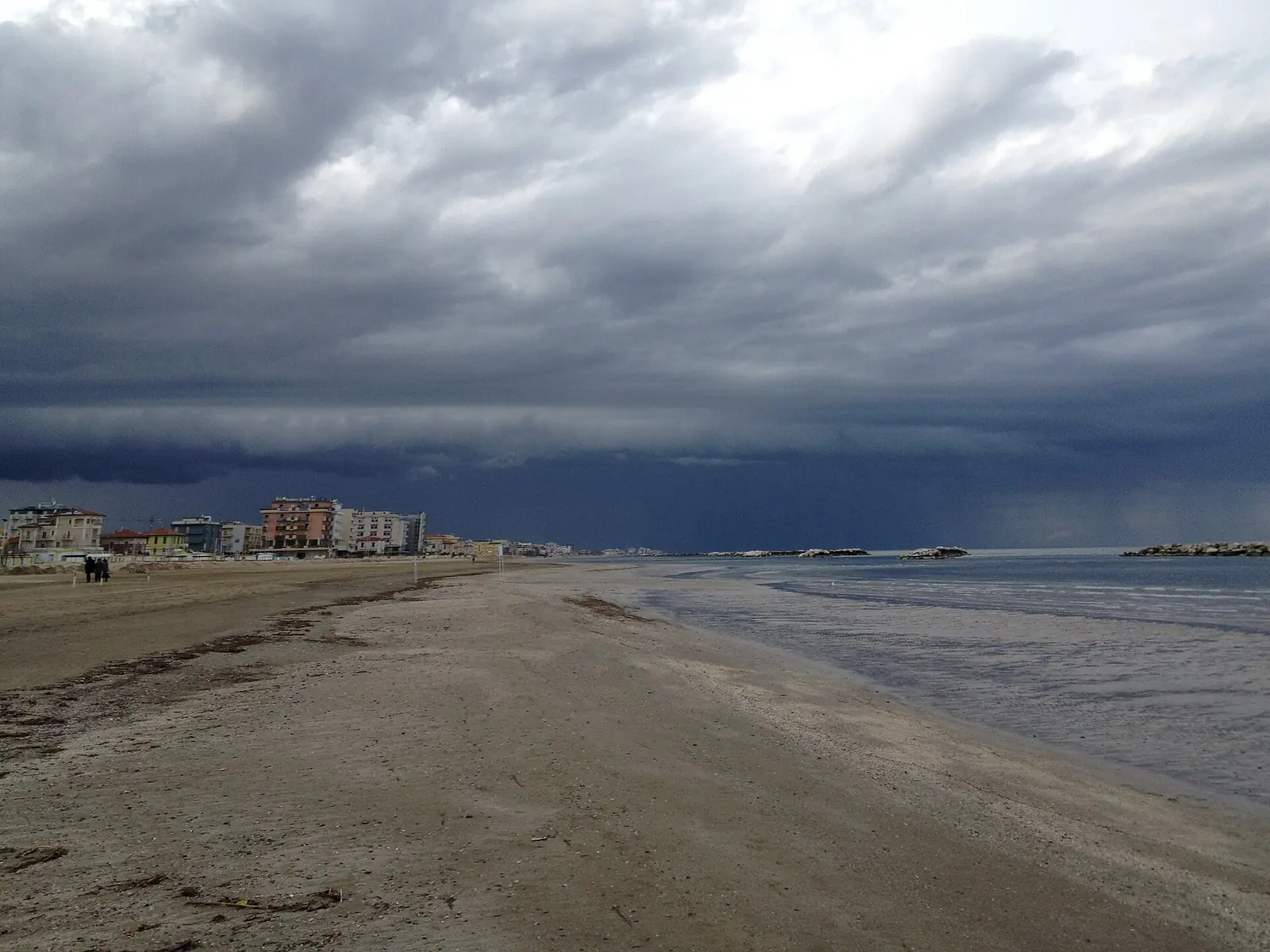 Der Strand von Rimini unter Gewitterhimmel mit verlassenem Ufer, drei Personen in der Ferne und Wellenbrechern