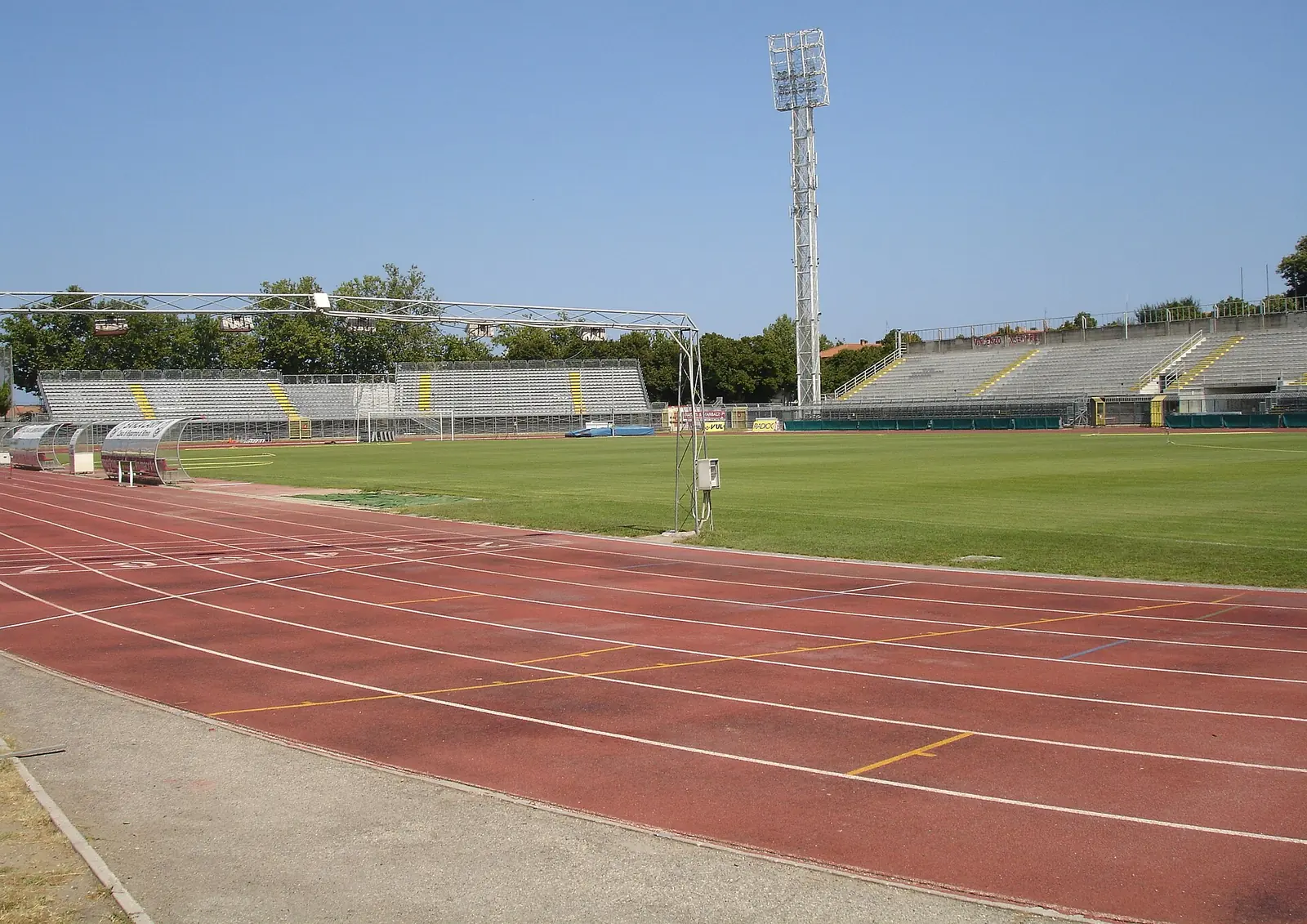 The red tartan track and grass pitch of Stadio Romeo Neri in Rimini, with empty stands and a floodlight tower