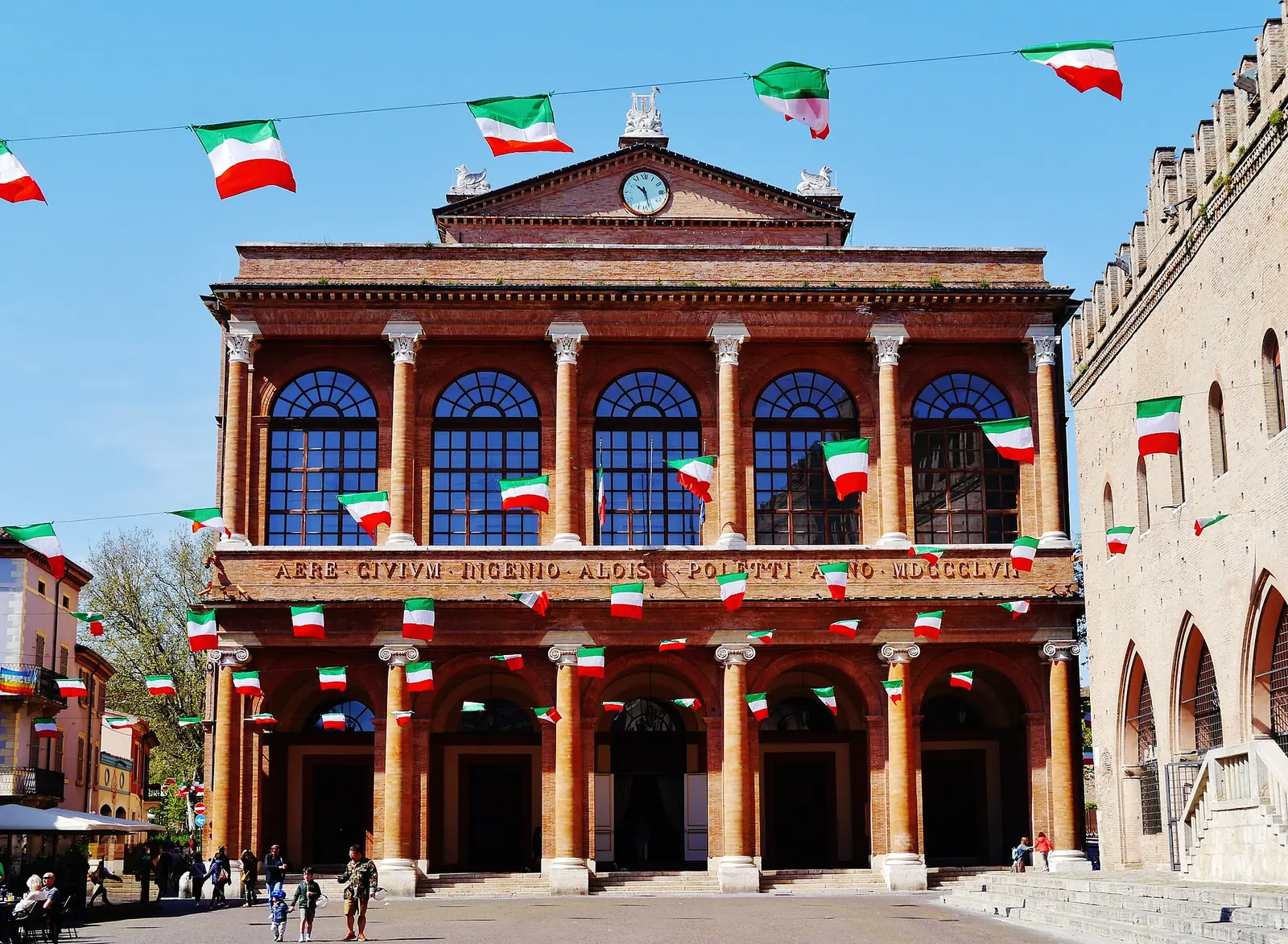 The brick façade of Teatro Amintore Galli in Piazza Cavour, Rimini, with Italian flags hanging outside