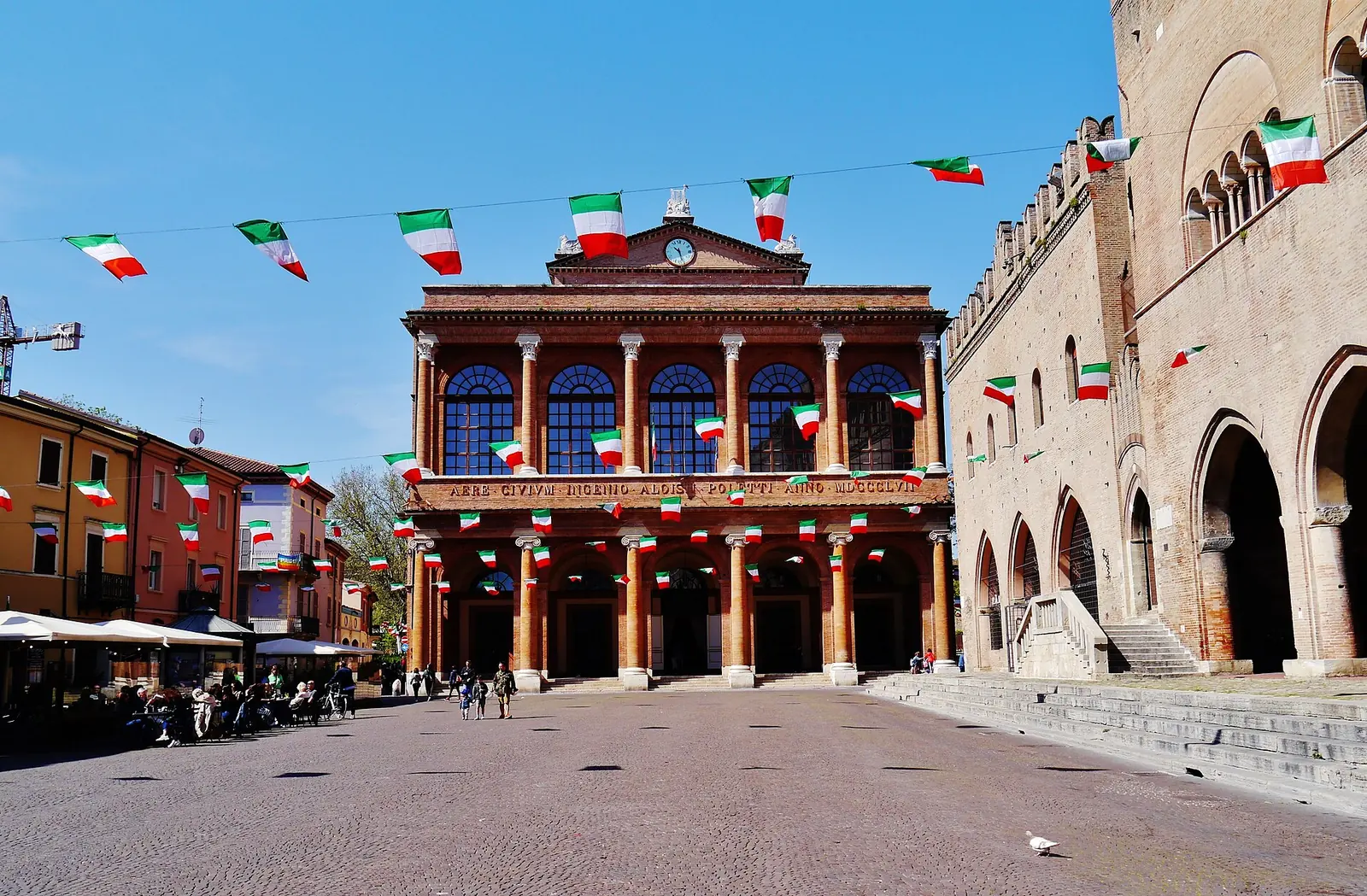 La facciata in mattoni del teatro in piazza Cavour a Rimini, con bandierine tricolori e il palazzo dell'Arengo a destra