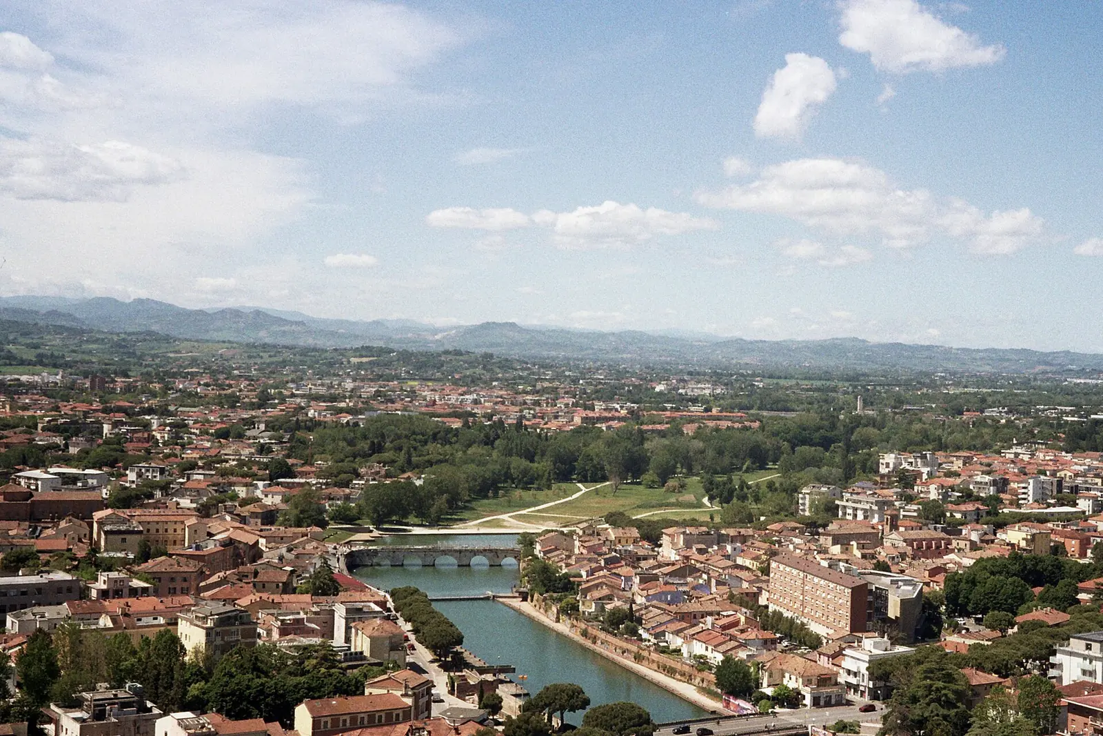 Rimini dall'alto, con il Ponte di Tiberio sul canale, il parco lungo l'antico alveo del Marecchia e le colline sullo sfondo