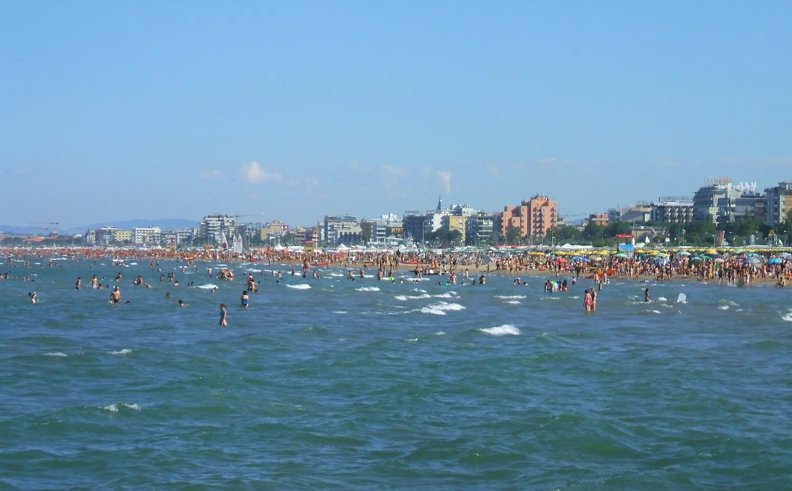 Il mare di Rimini d'estate, con i bagnanti e i palazzi del lungomare: il Boabay viene ancorato davanti a Marina Centro
