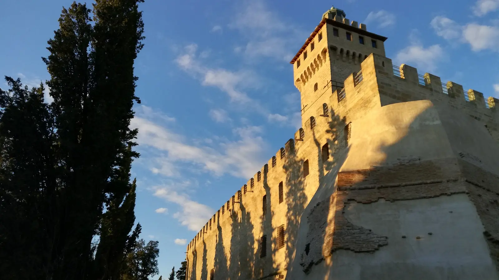 La torre e le mura merlate della Rocca delle Caminate illuminate dal sole, con i cipressi a sinistra