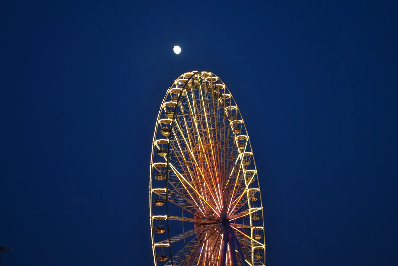 La partie supérieure de la grande roue de Rimini éclairée sur le ciel bleu du soir, avec la lune au-dessus