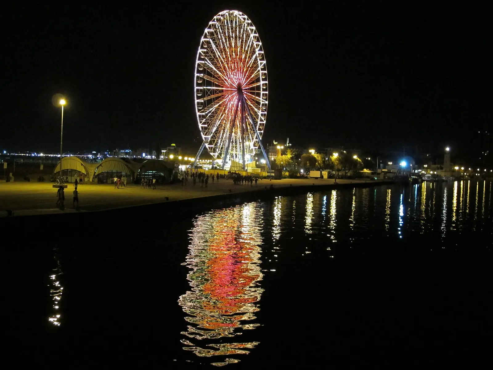 Rimini's observation wheel illuminated at night, with its colours reflected in the canal water