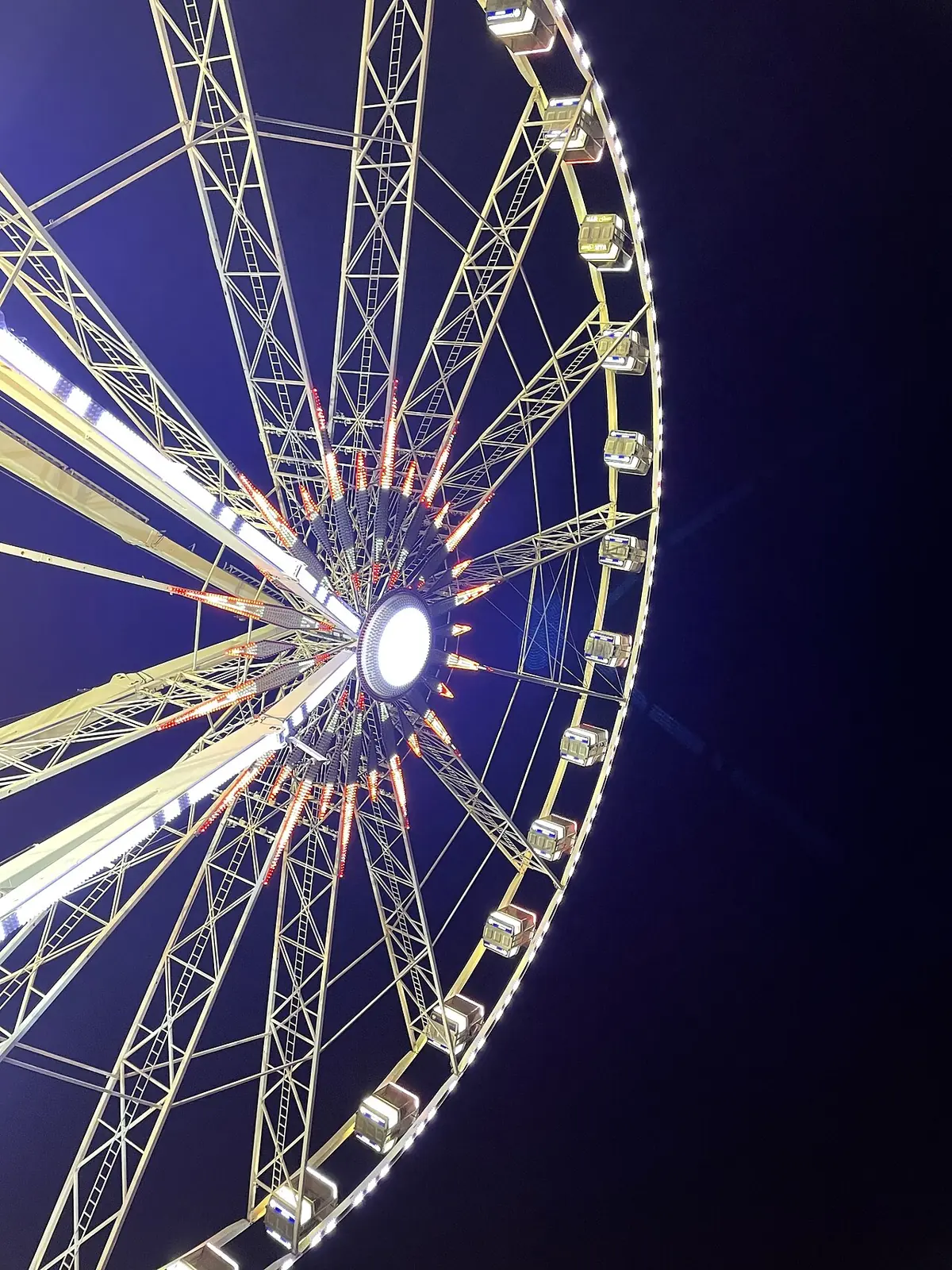 Le moyeu éclairé et les rayons de la grande roue de Rimini vus en contre-plongée la nuit, avec les cabines sur le pourtour