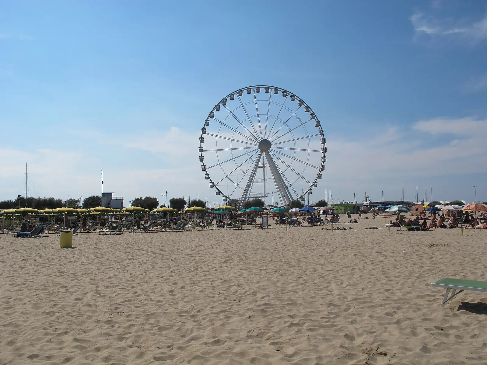 La ruota panoramica di Rimini sulla spiaggia, con la sabbia in primo piano e le file di ombrelloni sullo sfondo