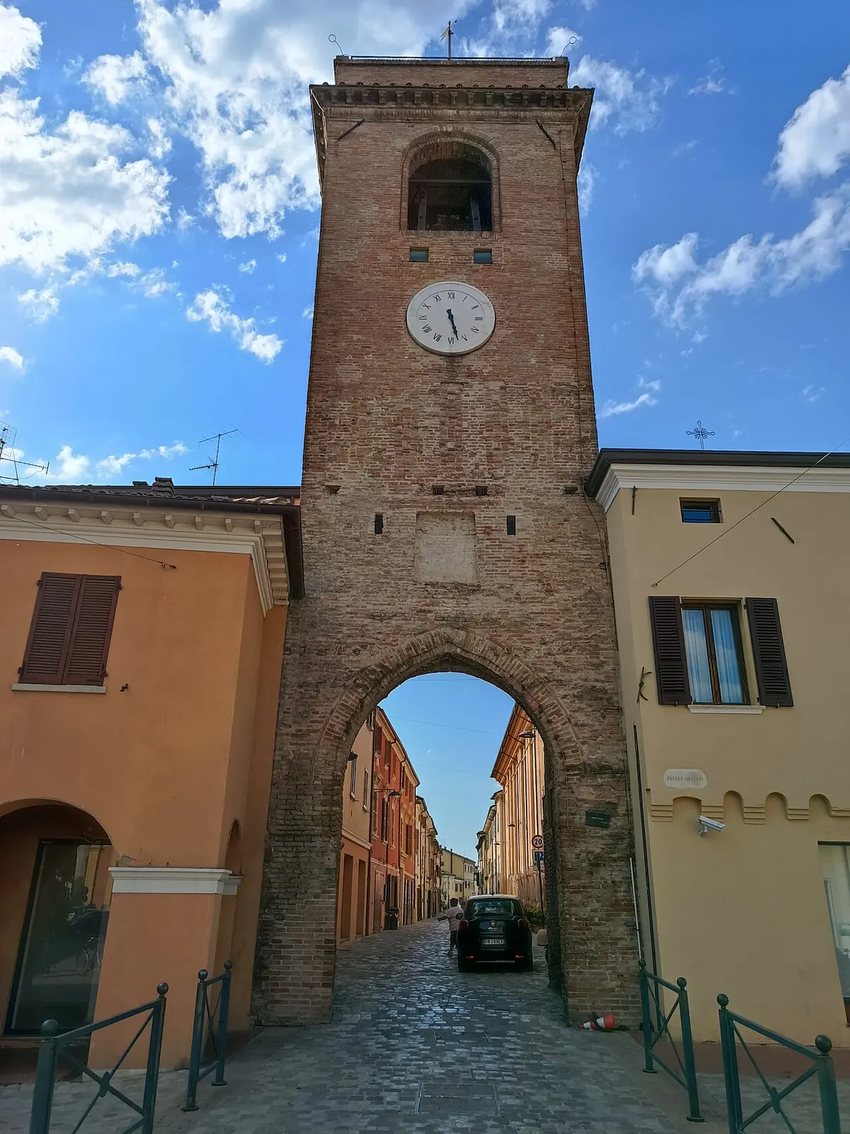 La torre civica con l'orologio e l'arco sulla strada a San Giovanni in Marignano, contro un cielo azzurro