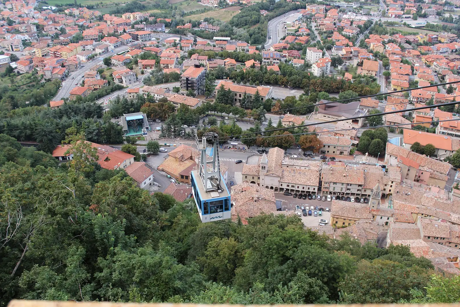 Une cabine du téléphérique de San Marino suspendue au-dessus des bois, avec les toits rouges de la localité en dessous