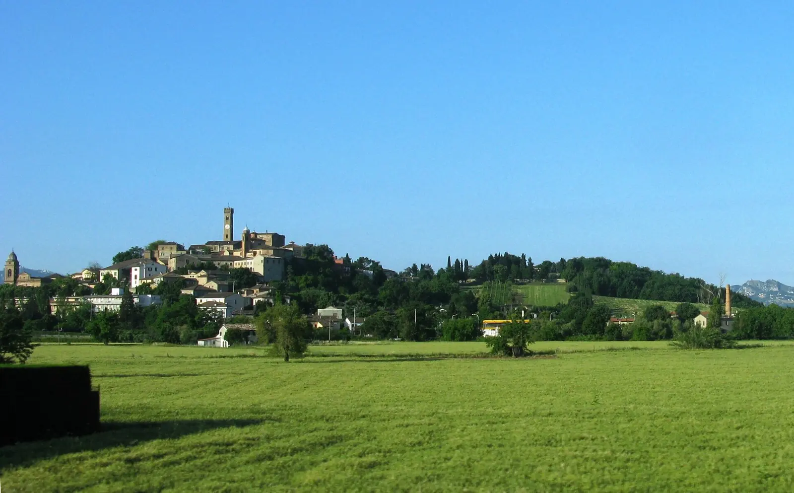 Die Altstadt von Santarcangelo di Romagna auf dem Hügel mit Türmen und Kirchtürmen, von einer grünen Wiese aus gesehen