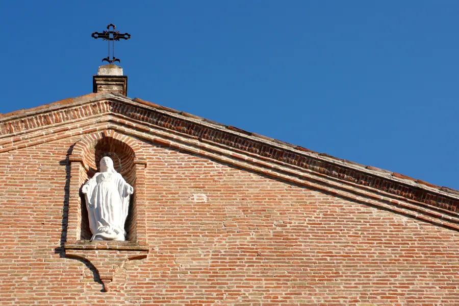 The brick pediment of Santuario di Santa Maria delle Grazie in Covignano, with its iron cross and Madonna statue