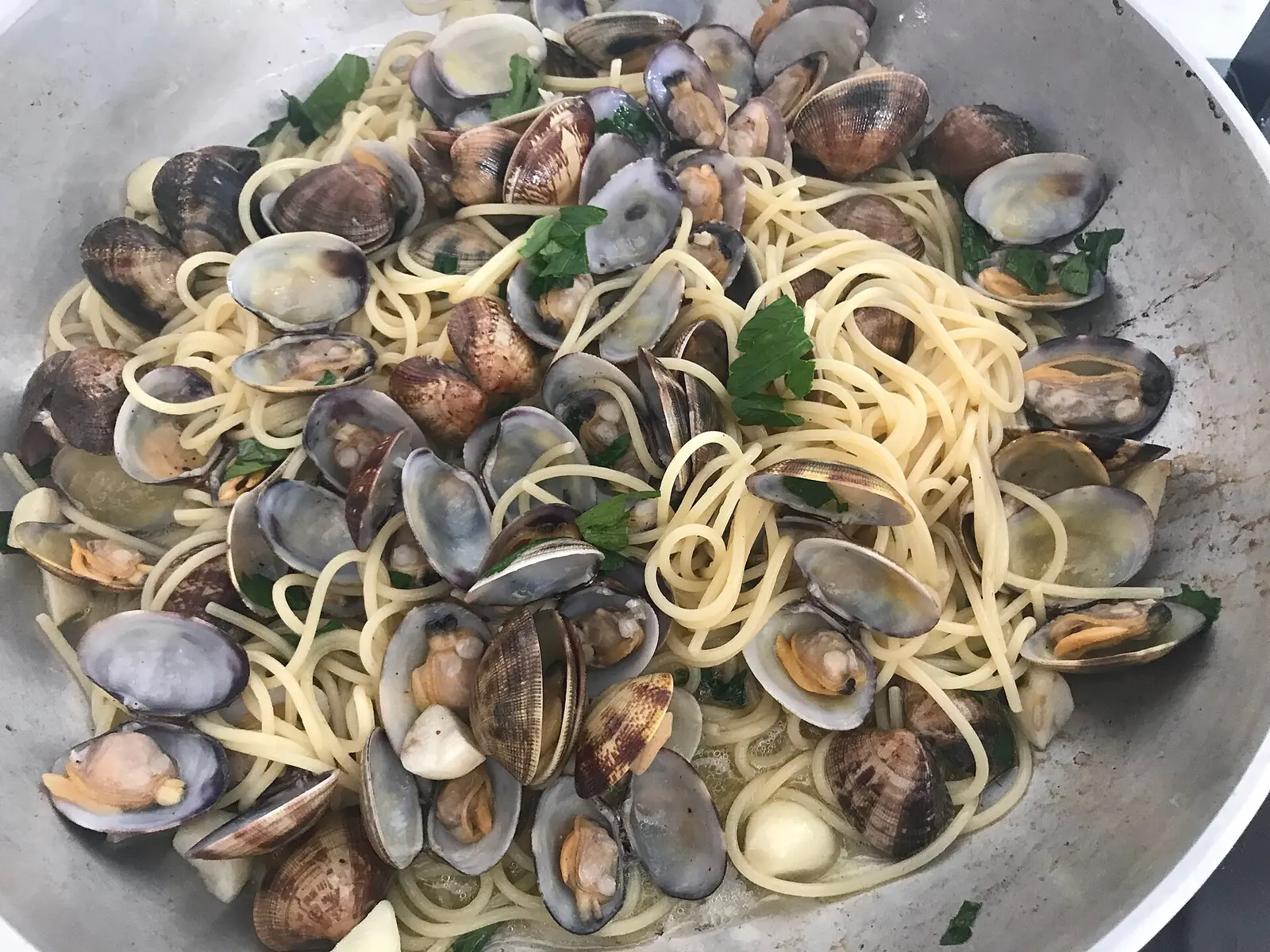 Spaghetti mit Venusmuscheln und Petersilie in einer Aluminiumpfanne mit Knoblauch und geöffneten Schalen
