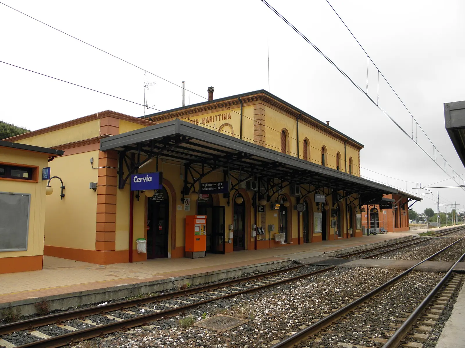 La stazione di Cervia-Milano Marittima, edificio giallo e arancione con la pensilina in ferro, vista dai binari