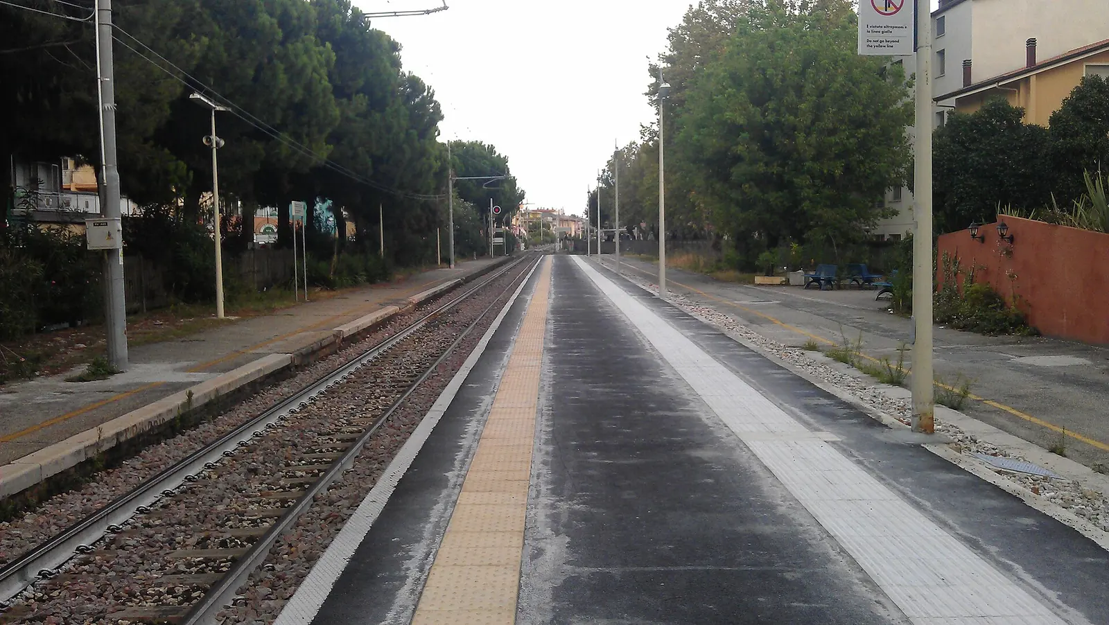 The platform and tracks at Bellaria station towards Rimini, among trees and houses