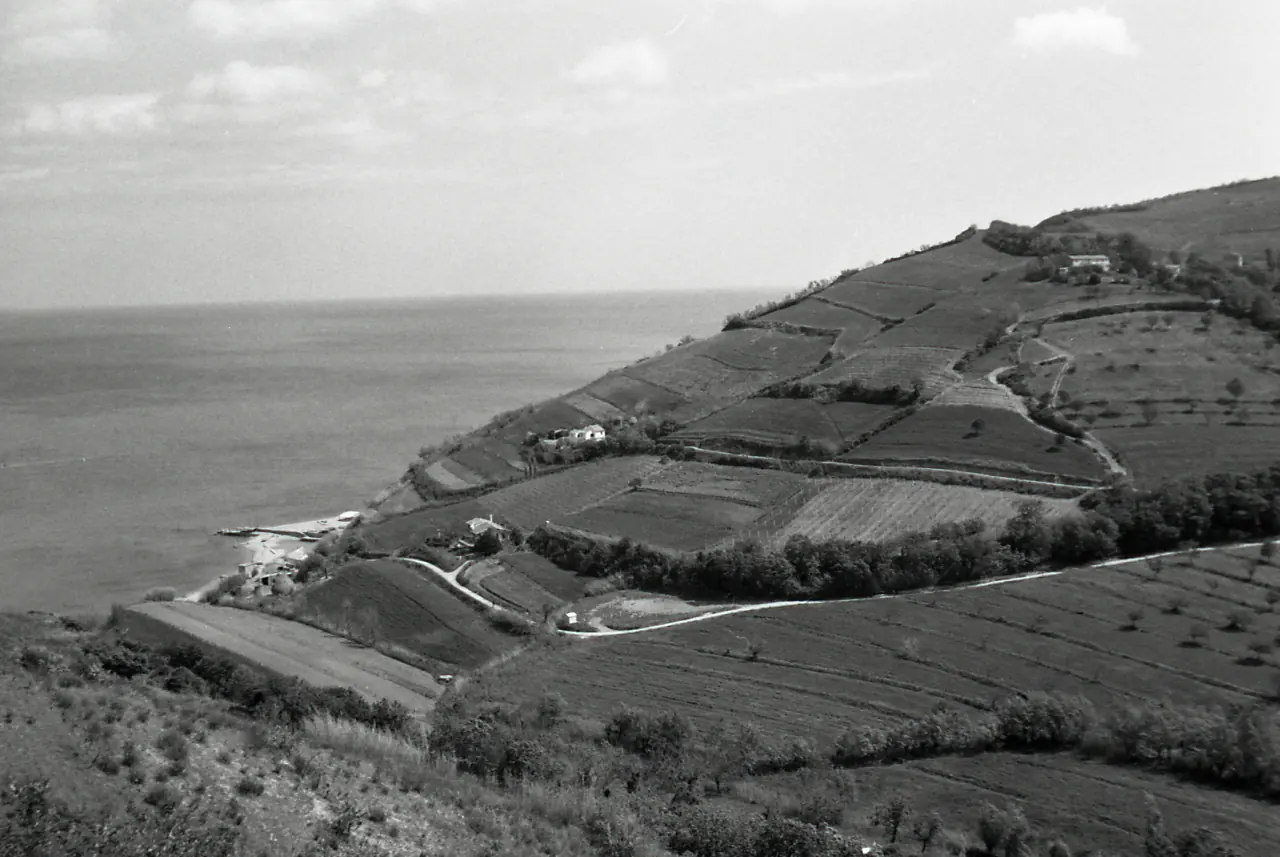Die Bucht von Vallugola von oben im Jahr 1968 mit einem kleinen Anlegeplatz am Ufer, terrassierten Feldern und einer Straße zum Meer