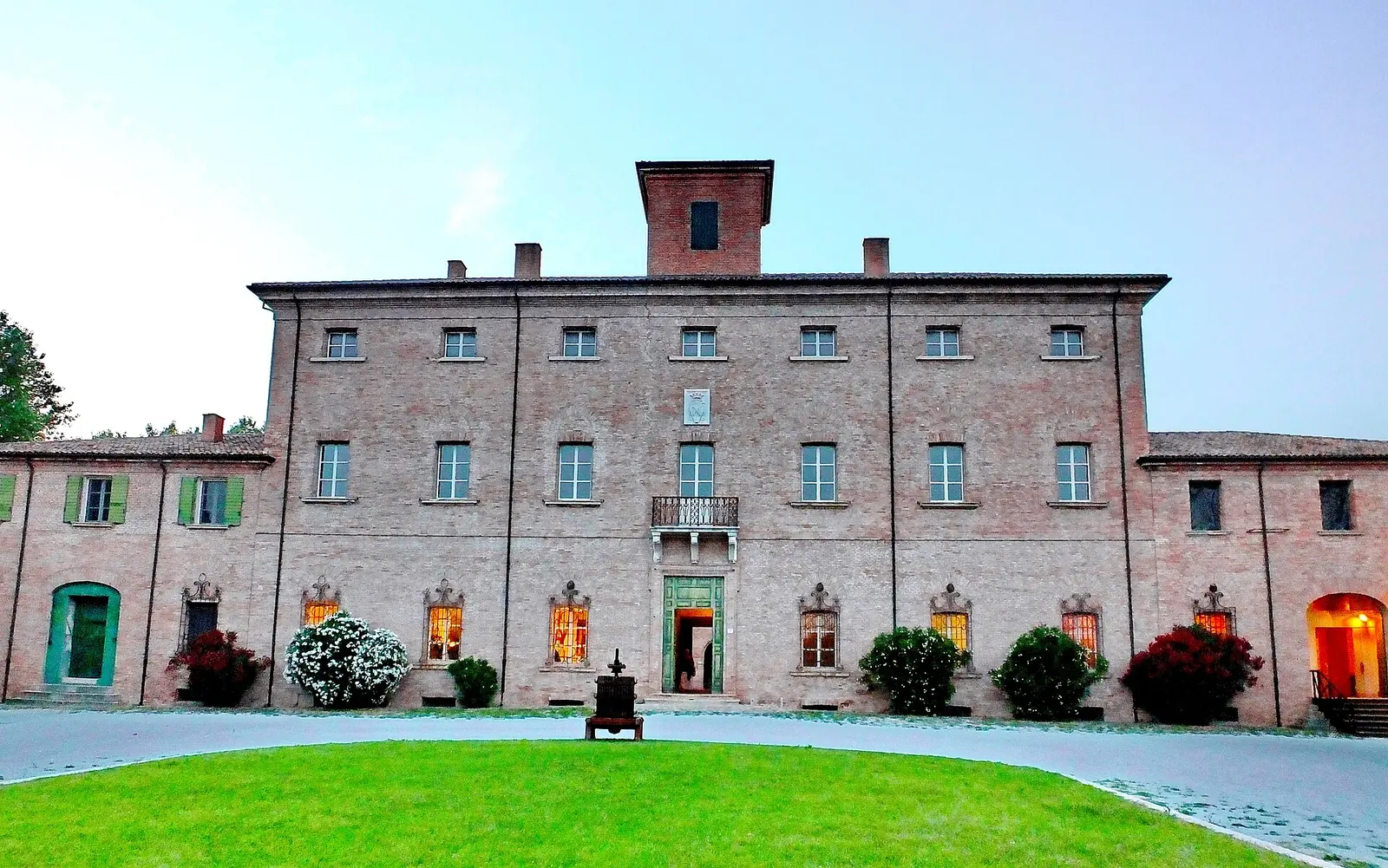 La facciata in mattoni di Villa Torlonia a San Mauro Pascoli, con il portale verde, la torretta e il prato davanti