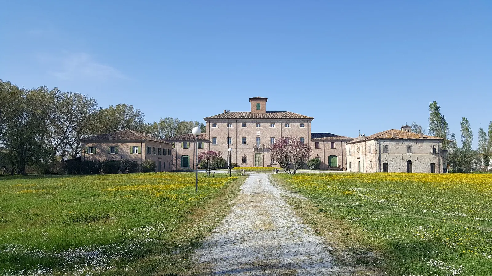 Il complesso di Villa Torlonia a San Mauro Pascoli visto da un sentiero di ghiaia che attraversa un prato fiorito