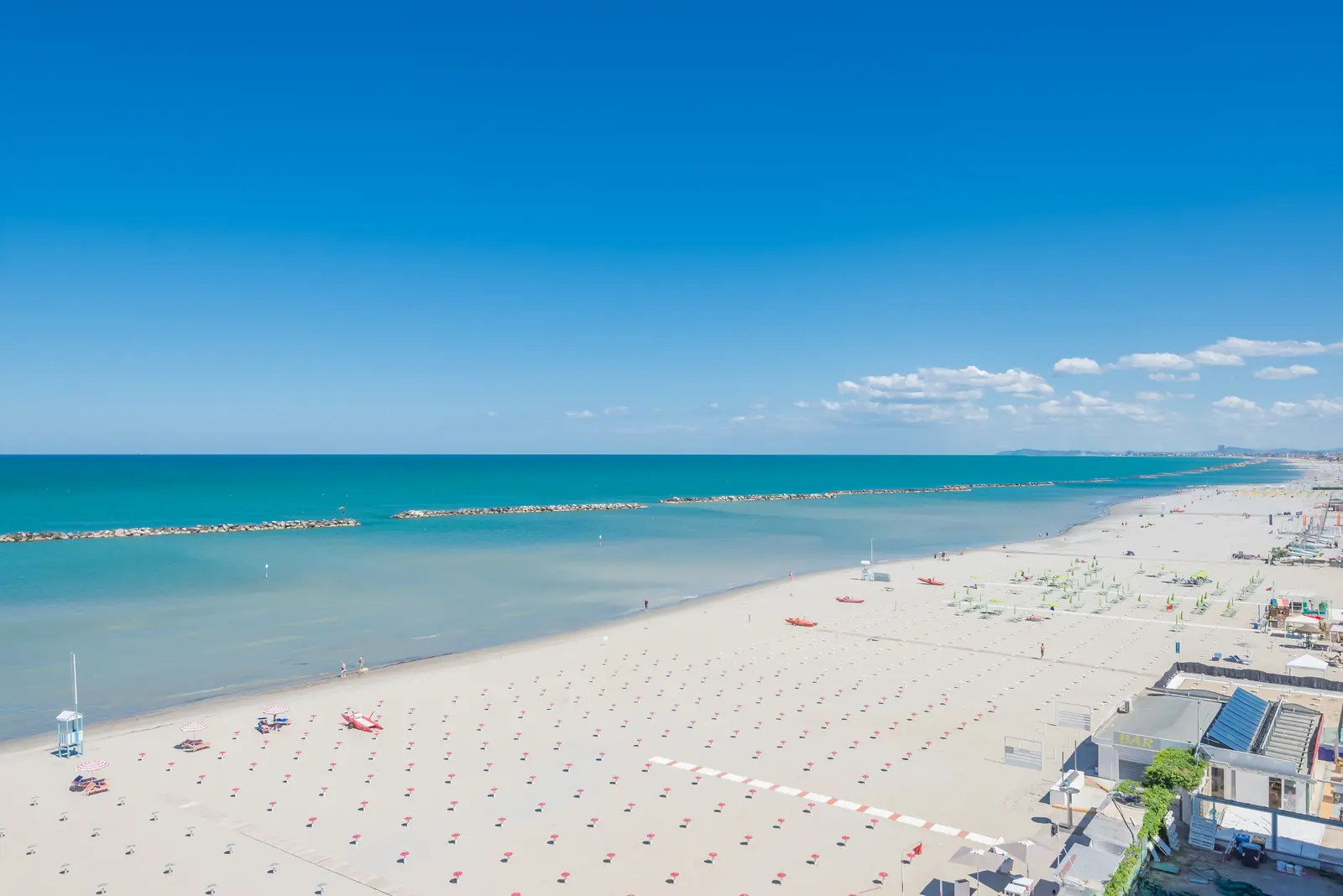 La spiaggia di Bellaria Igea Marina dall'alto, con il mare turchese, le scogliere e gli ombrelloni ancora chiusi