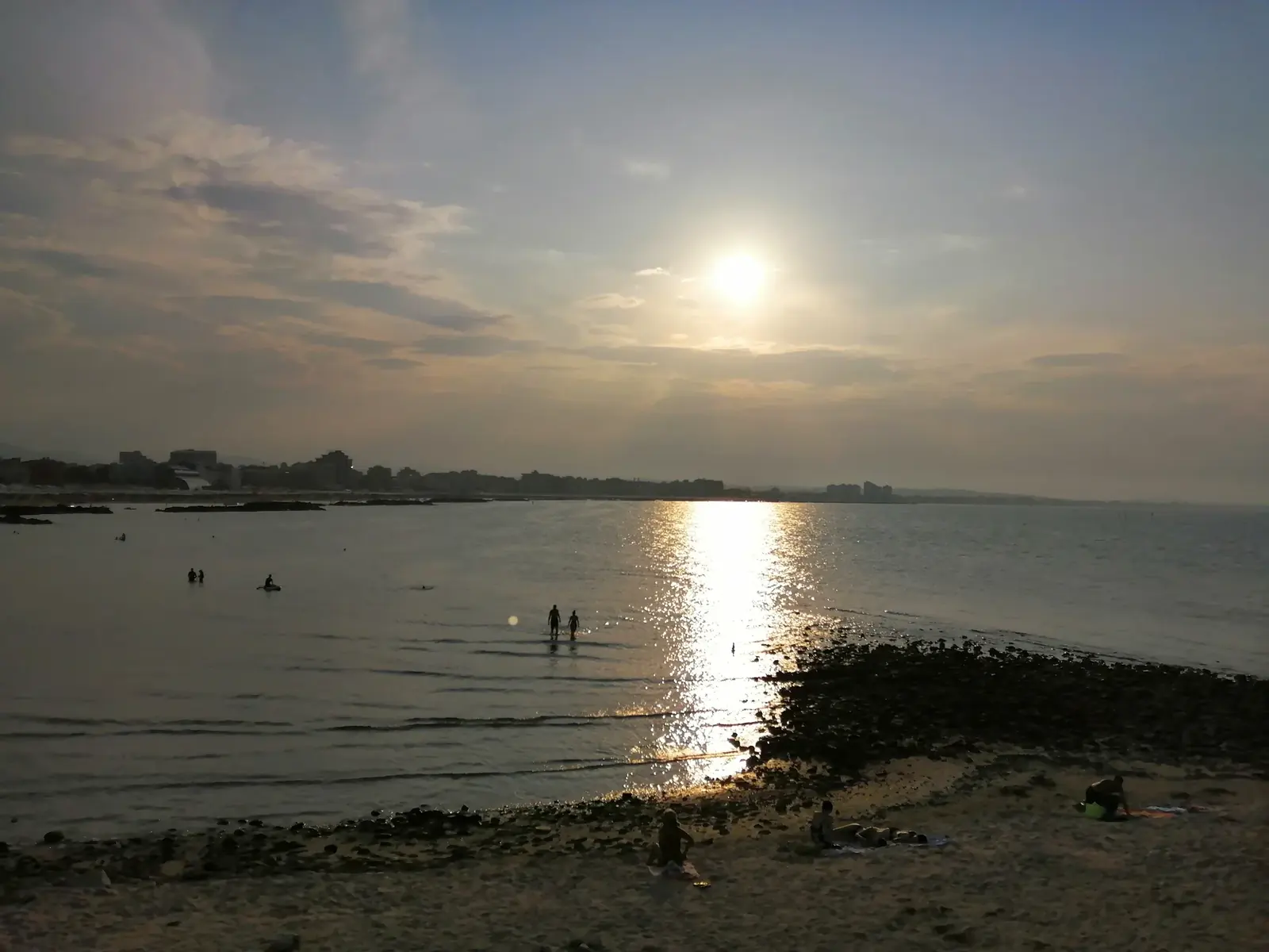 La spiaggia di Cattolica al tramonto, con il sole riflesso sul mare calmo e poche persone sulla battigia