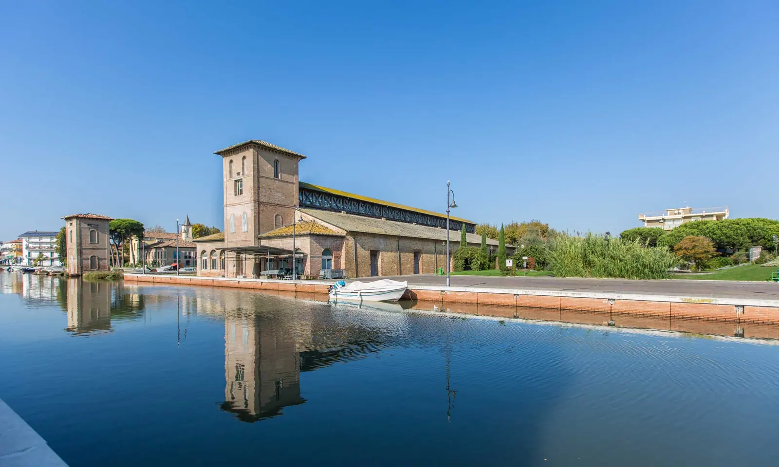 Il magazzino del sale di Cervia riflesso nell'acqua del canale, con la torre in mattoni e il prato
