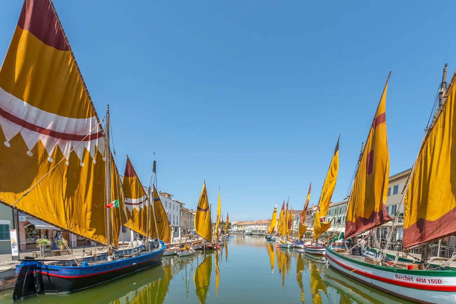 Le barche storiche con le vele al terzo gialle e rosse nel porto canale di Cesenatico, con le case sulle banchine