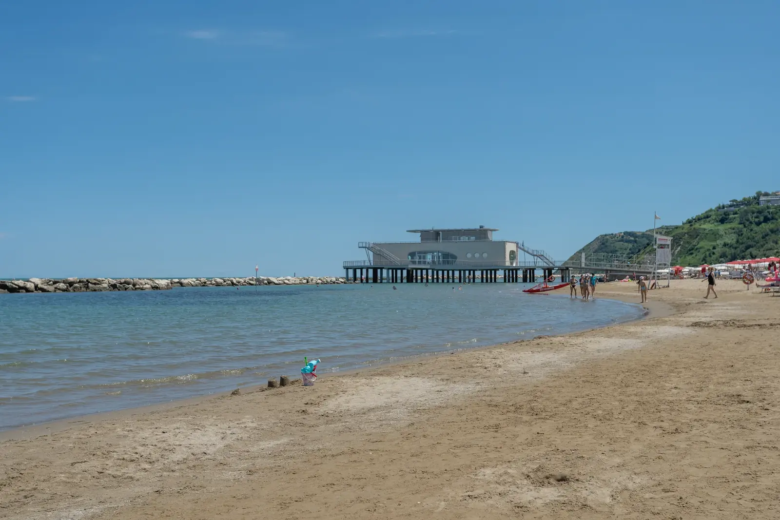 La spiaggia di Gabicce Mare con la sabbia bagnata, l'acqua bassa e il pontile sullo sfondo