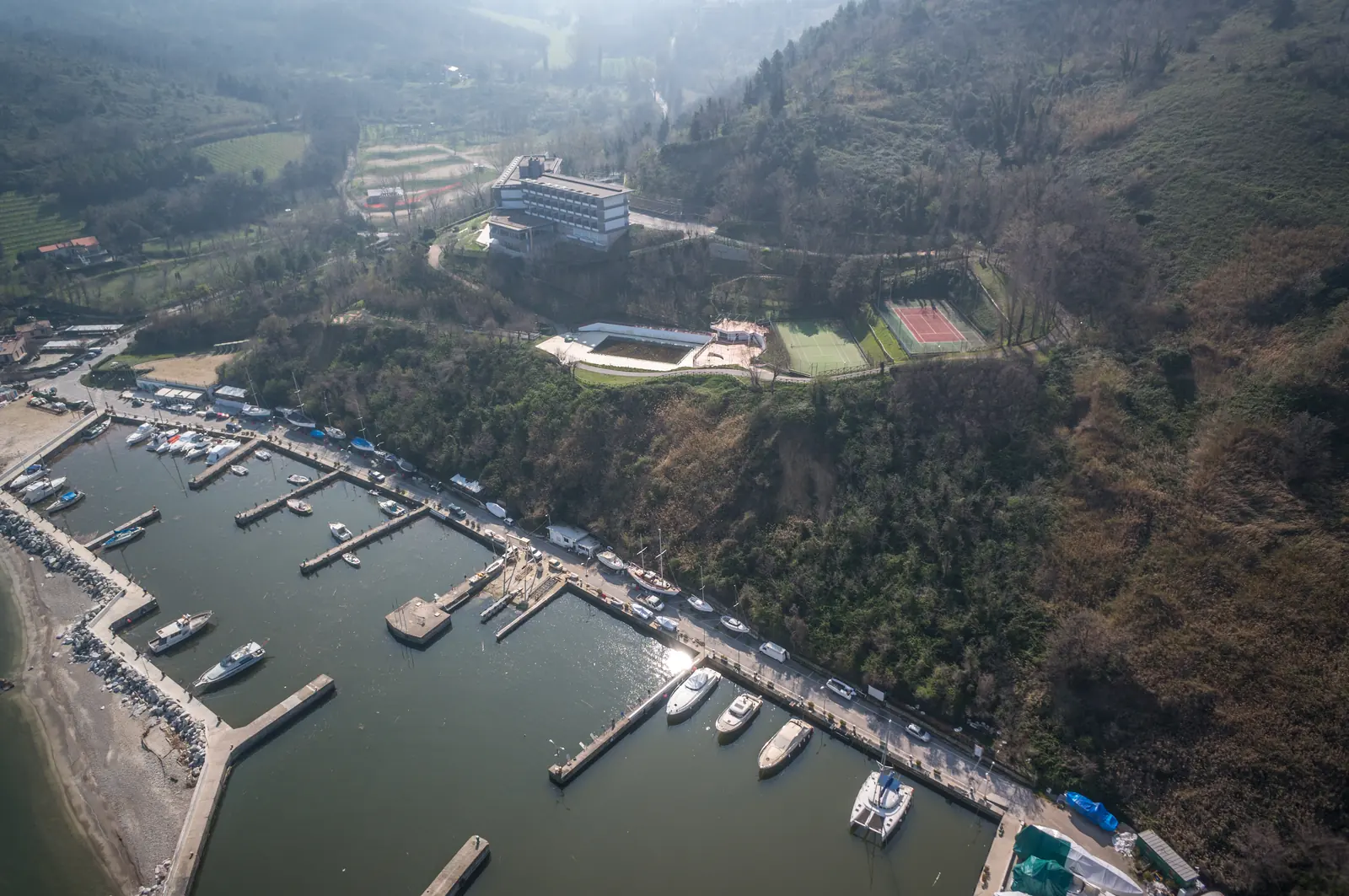 Il porto di Vallugola visto dall'alto, con le barche ai pontili sotto il promontorio boscoso