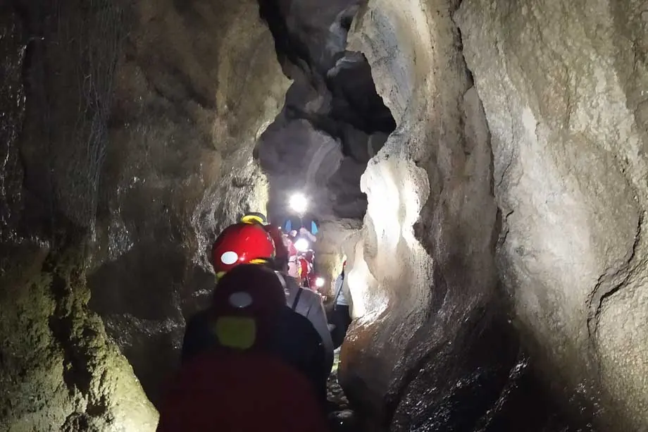 Visitatori con il casco da speleologo in fila in uno stretto passaggio della grotta di Onferno, fra pareti di roccia chiara