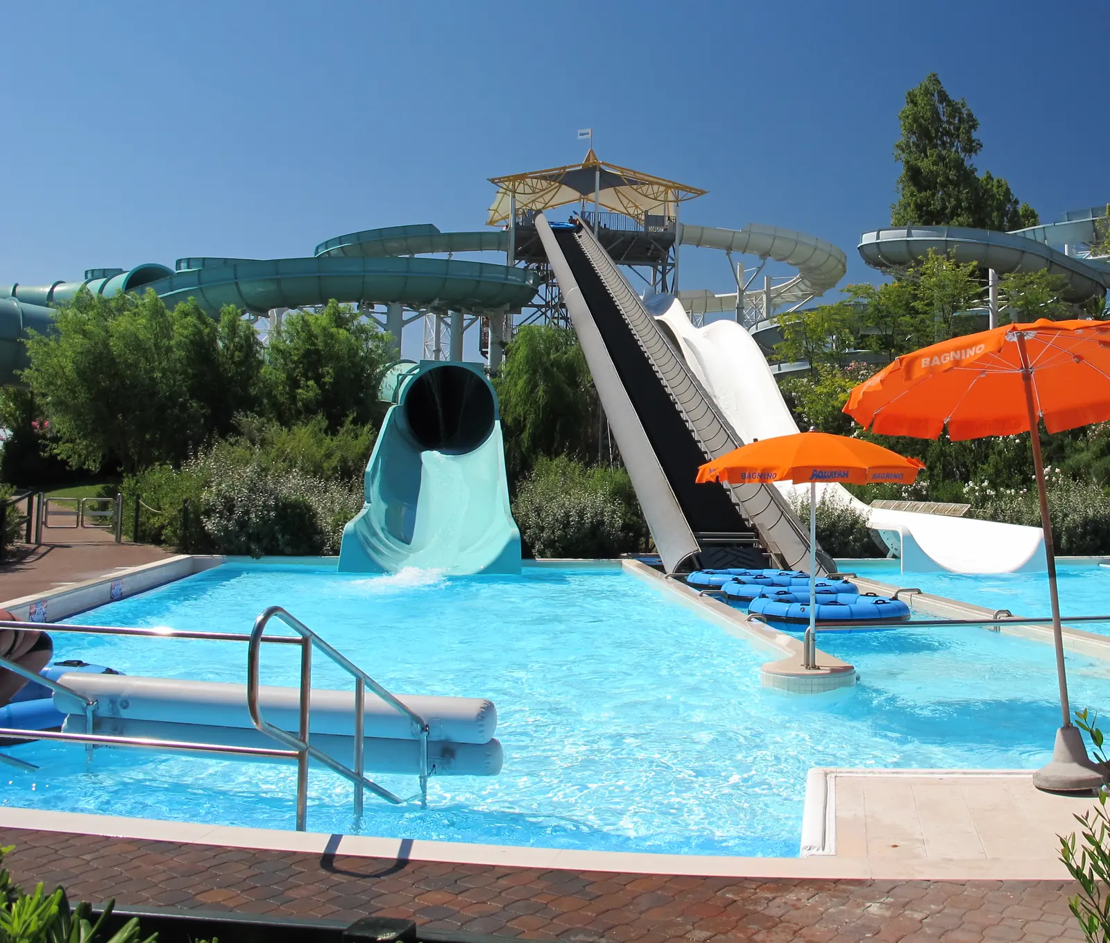 Scivoli e tubi verdi sopra una piscina azzurra dell'Aquafan di Riccione, con due ombrelloni arancioni e gli alberi