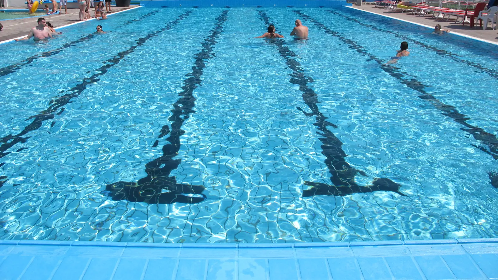 La piscina a corsie vista dal bordo, con le righe sul fondo e pochi bagnanti lontani