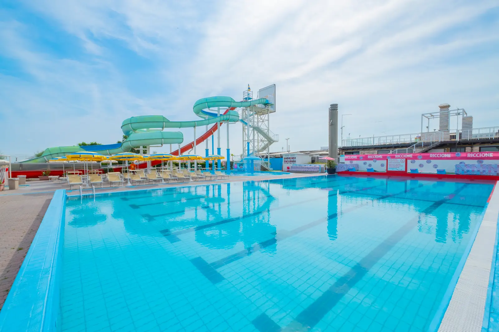 La piscina a corsie del Beach Village con gli scivoli verdi e rossi, i lettini e gli ombrelloni gialli sul bordo