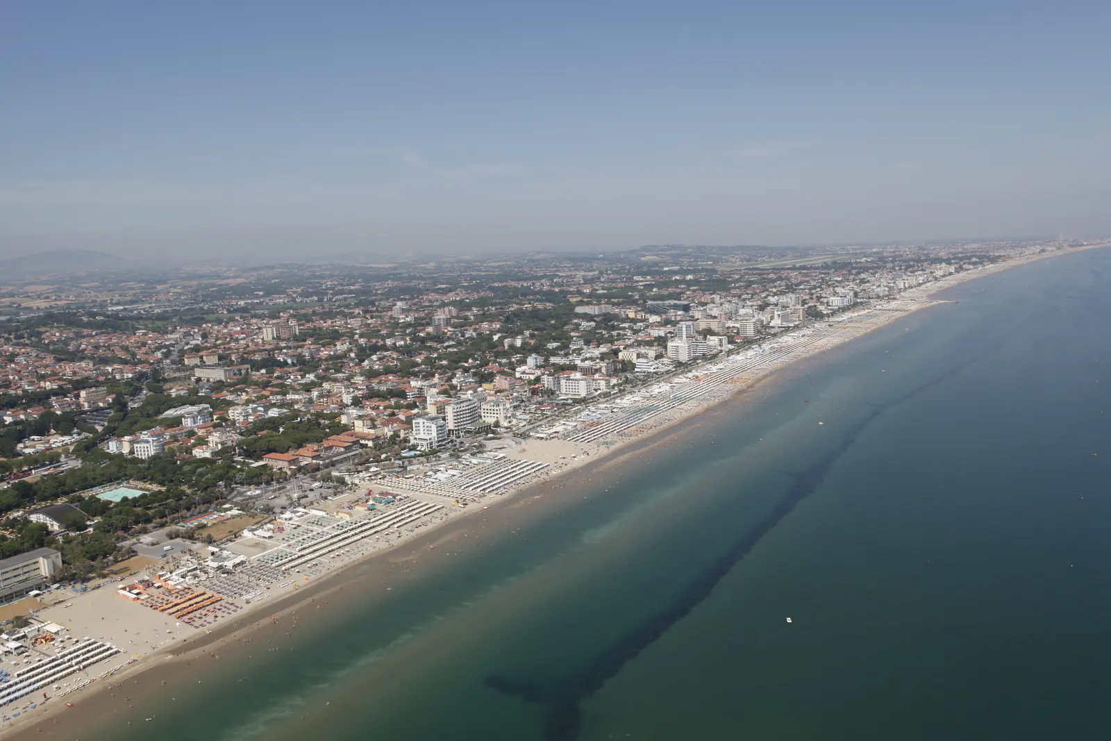 La costa di Riccione vista dall'alto verso nord, con la lunga spiaggia, la città fino alle colline e il mare verde