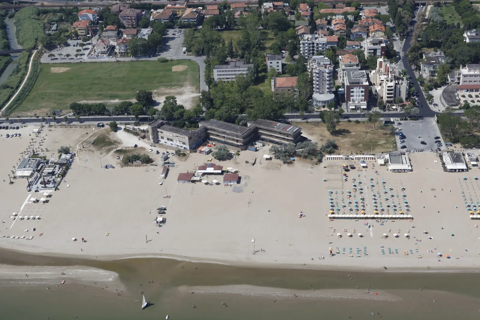 La spiaggia larga alla foce del Marano vista dall'alto, con il torrente a sinistra e pochi ombrelloni sulla sabbia