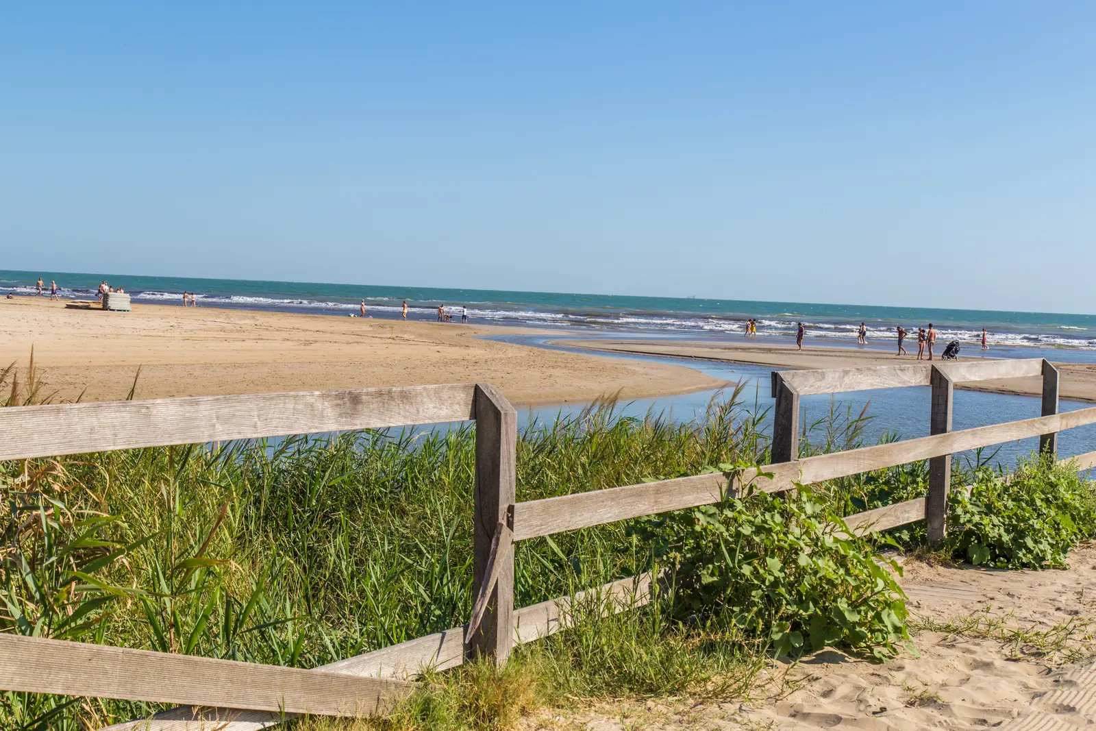La staccionata di legno fra le canne alla foce del Marano a Riccione, con la spiaggia libera e il mare mosso