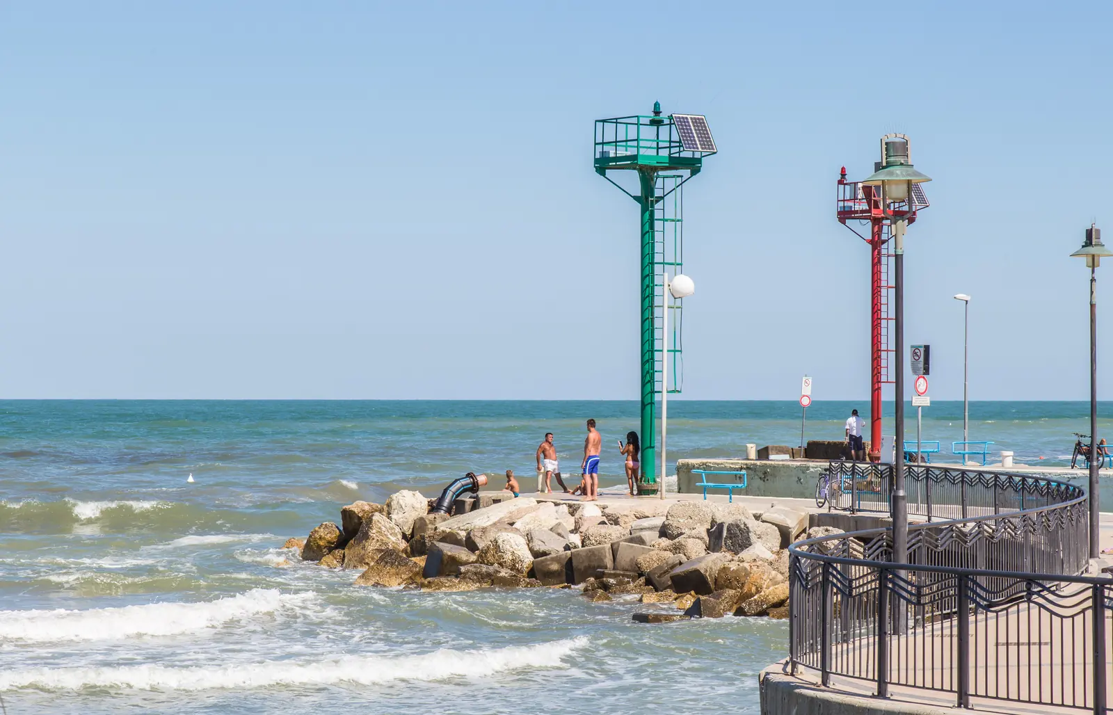 I fanali verde e rosso alla testata del molo di Riccione, con la scogliera, il mare mosso e la passeggiata curva